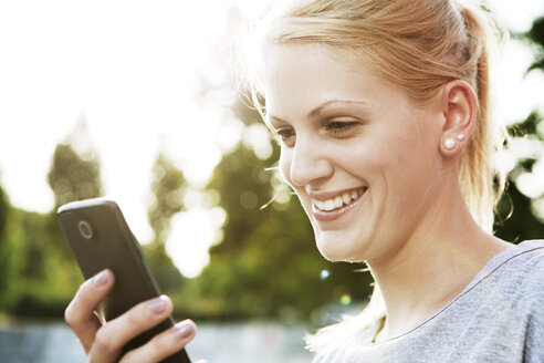 Lächelnde junge Frau mit Smartphone - FEXF000033