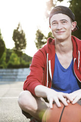 Young man with basketball sitting on ground - FEXF000047