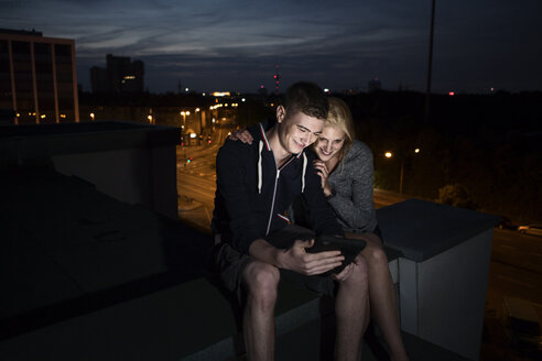 Young couple with tablet pc sitting on flat roof by night - FEXF000005