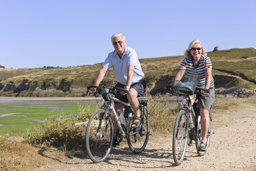 Frankreich, Bretagne, Finistere, Seniorenpaar auf E-Bikes an der Küste - LA000148