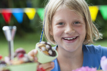 Glückliches Mädchen isst Muffin auf einer Geburtstagsparty - NHF001434