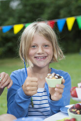 Glückliches Mädchen isst Muffin auf einer Geburtstagsparty - NHF001448