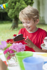 Glücklicher Junge hält Teller mit Kuchen auf einer Geburtstagsparty - NHF001452