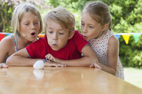 Kinder blasen Wattebausch auf Gartentisch, lizenzfreies Stockfoto