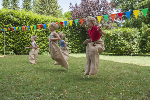 Kinder machen ein Sackhüpfen im Garten auf einer Geburtstagsfeier - NHF001462