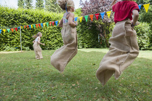 Kinder machen ein Sackhüpfen im Garten auf einer Geburtstagsfeier - NHF001461