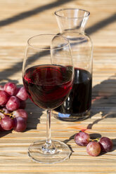 Glas und Karaffe mit Rotwein und roten Trauben am Holztisch - SARF000105