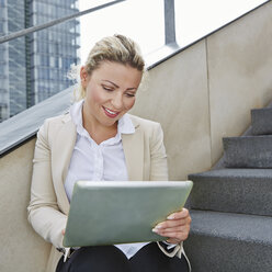 Deutschland, Köln, Geschäftsfrau auf Treppe sitzend, mit digitalem Tablet - RKNF000138