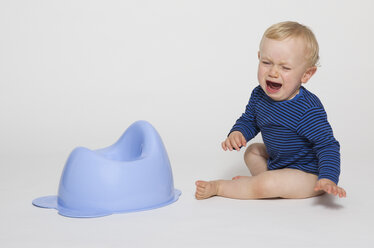 Crying baby boy sitting next to his potty, studio shot - MUF001388