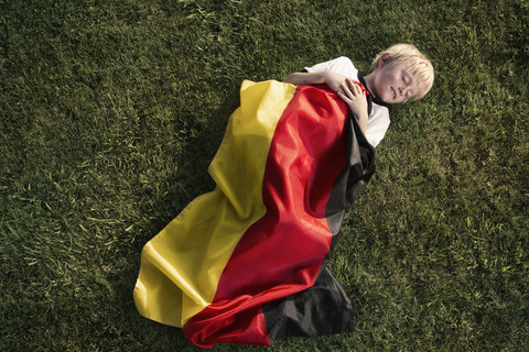 Deutschland, Köln, Junger Fußballfan schläft eingewickelt in die deutsche Flagge, lizenzfreies Stockfoto