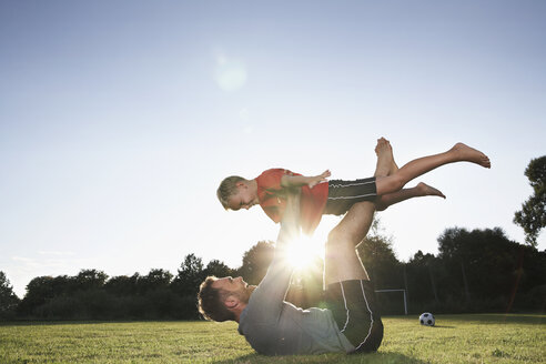 Germany, Cologne, Father holding son aloft on soccer field - PDF000422