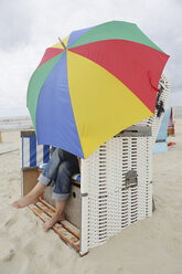 Deutschland, Niedersachsen, Ostfriesland, Langeoog, Frau mit offenem Schirm im überdachten Strandkorb sitzend - JATF000311