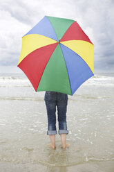 Deutschland, Niedersachsen, Ostfriesland, Langeoog, Frau mit offenem Regenschirm am Strand stehend - JATF000313