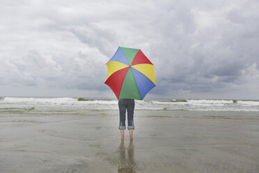 Deutschland, Niedersachsen, Ostfriesland, Langeoog, Frau mit offenem Regenschirm am Strand stehend - JATF000314