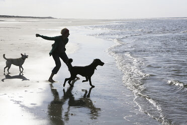 Deutschland, Niedersachsen, Ostfriesland, Langeoog, Frau spielt mit ihren Hunden am Strand - JATF000348