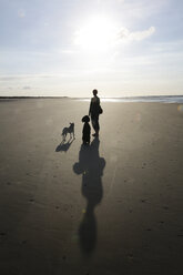Deutschland, Niedersachsen, Ostfriesland, Langeoog, Schatten und Silhouetten einer Frau und ihrer Hunde am Strand - JATF000360