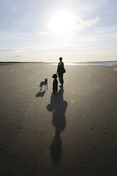 Germany, Lower Saxony, East Frisia, Langeoog, shadows and silhouettes of a woman and her dogs at the beach - JATF000360