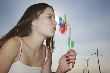 Germany, North Rhine-Westphalia, Neuss, Teenage girl with pinwheel in front of wind farm - JATF000361