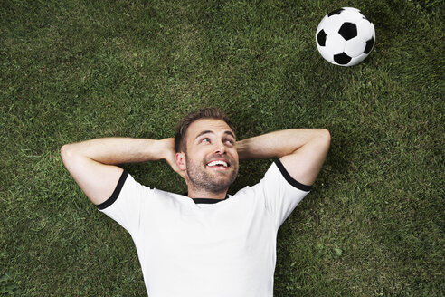 Deutschland, Junger Mann liegt auf Rasen und schaut Fußball - PDF000437