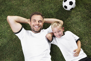 Germany, Father and sun lying on lawn, wearing football shirts - PDF000438