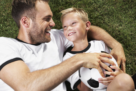 Germany, Father and sun lying on lawn, wearing football shirts stock photo
