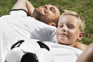 Deutschland, Vater und Sonne auf dem Rasen liegend, in Fußballtrikots - PDF000440