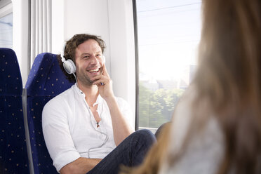 Man with headphones in a train smiling at woman - KFF000257