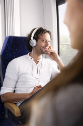 Man with headphones in a train smiling at woman - KFF000256