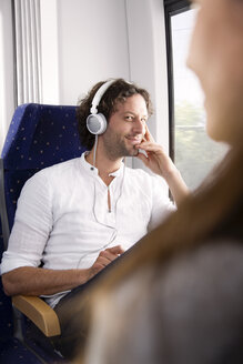Mann mit Kopfhörern in einem Zug lächelt Frau an - KFF000256