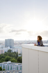 Germany, Berlin, Young woman on rooftop terrace, looking at view - FKF000271