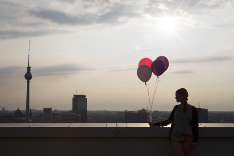 Deutschland, Berlin, Junge Frau auf Dachterrasse, hält Luftballons, lizenzfreies Stockfoto