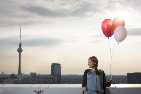 Deutschland, Berlin, Junge Frau auf Dachterrasse, hält Luftballons - FKF000283