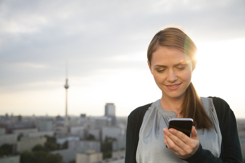 Germany, Berlin, Young woman on rooftop terrace, using mobile phone stock photo