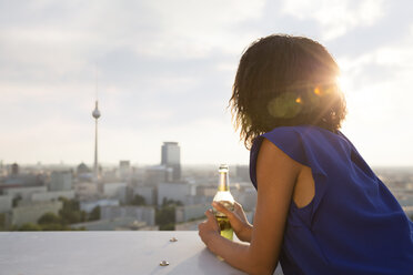 Germany, Berlin, Young woman looking at view, holding beer bottle - FKF000289