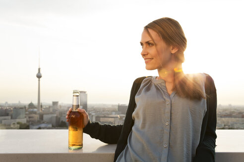 Germany, Berlin, Young woman on rooftop terrace, drinking beer - FKF000290