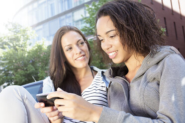 Deutschland, Berlin, Junge Frauen in der Stadt, die ein Mobiltelefon benutzen - FKF000291