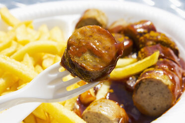 Currywurst auf Gabel mit Pommes im Hintergrund - CSF020041