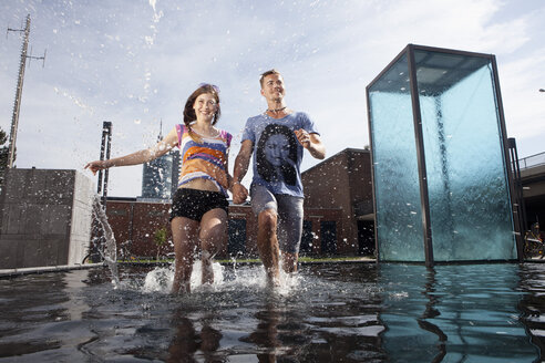 Germany, Bavaria, Munich, Couple running through water at fountain - RBF001359