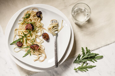 Plate with fig tagliatelle, rocket leaves, sauce and a glass of water, studio shot - SBDF000222