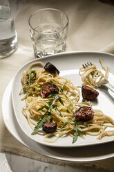 Plate with fig tagliatelle, rocket leaves, sauce and a glass of water, studio shot - SBDF000223