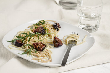 Plate with fig tagliatelle, rocket leaves, sauce and a glass of water, studio shot - SBDF000225