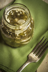 Eingelegte und in Scheiben geschnittene Jalapeno-Chilis (Capsicum annuum) in einem Glas, grüne Serviette und Gabel, Studioaufnahme - SBD000226