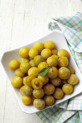 Mirabelles (Prunus domestica subsp. syriaca) in a bowl on wooden table, studio shot - CSF020090