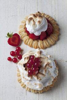 Two meringue tartlets with red currants and strawberries on wood, studio shot - CSF020095