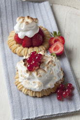 Two meringue tartlets with red currants and strawberries on wood, studio shot - CSF020097