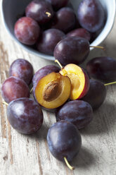 Pflaumen (Prunus domestica) in einer Schale und auf einem Holztisch, Studioaufnahme - CSF020110