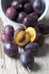 Plums (Prunus domestica) in a bowl and on wooden table, studio shot - CSF020110