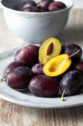 Teller und Schale mit Pflaumen (Prunus domestica) auf Holztisch, Studioaufnahme - CSF020111