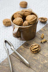 Earthenware jar with walnuts (Juglans regia) and nutcracker on wooden table, studio shot - LVF000226