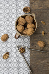 Earthenware jar with walnuts (Juglans regia) and nutcracker on wooden table, studio shot - LVF000230